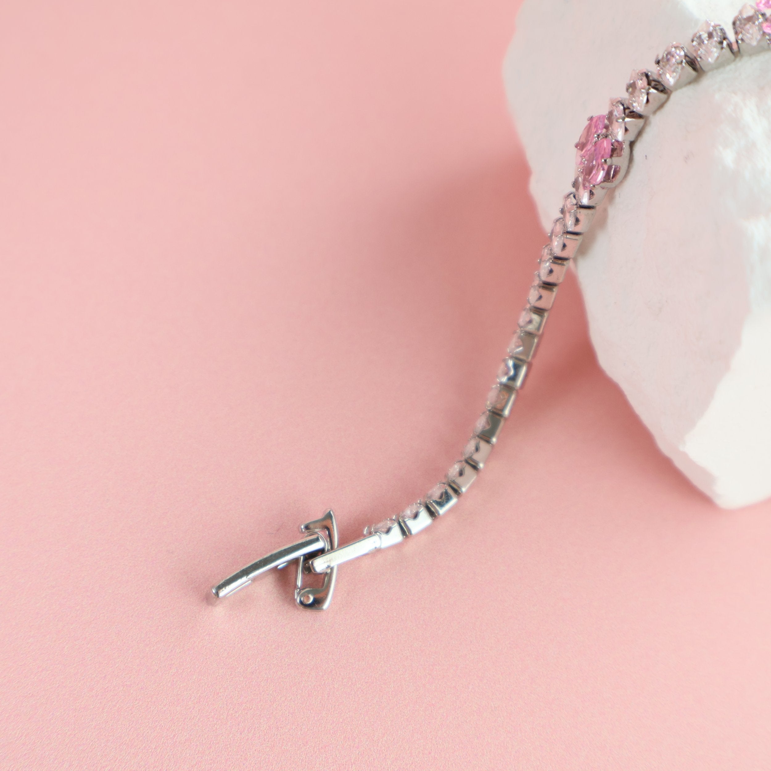 Silver and pink zirconia bracelet displayed on textured white prop